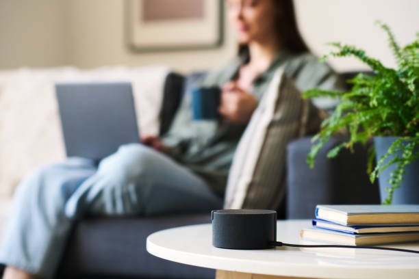 A smart speaker on a table with a person relaxing on a couch in the background.