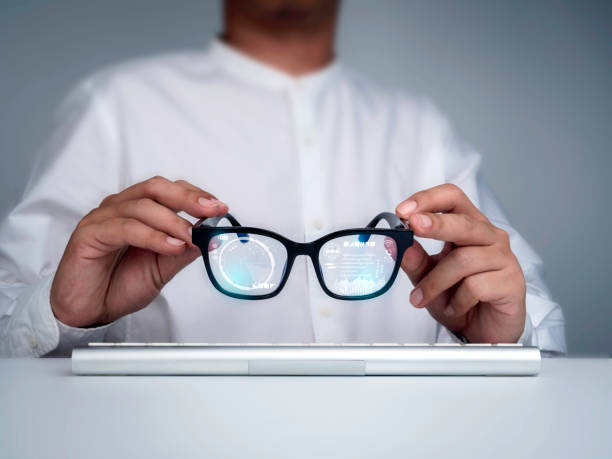 A person holding smart glasses with digital interfaces reflected on the lenses above a keyboard.